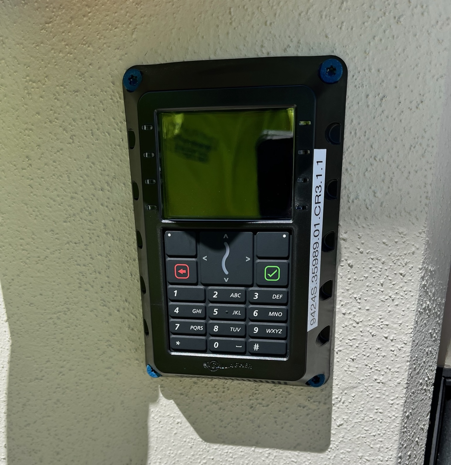 Wall-mounted keypad reader with LCD display installed on an exterior stucco wall.