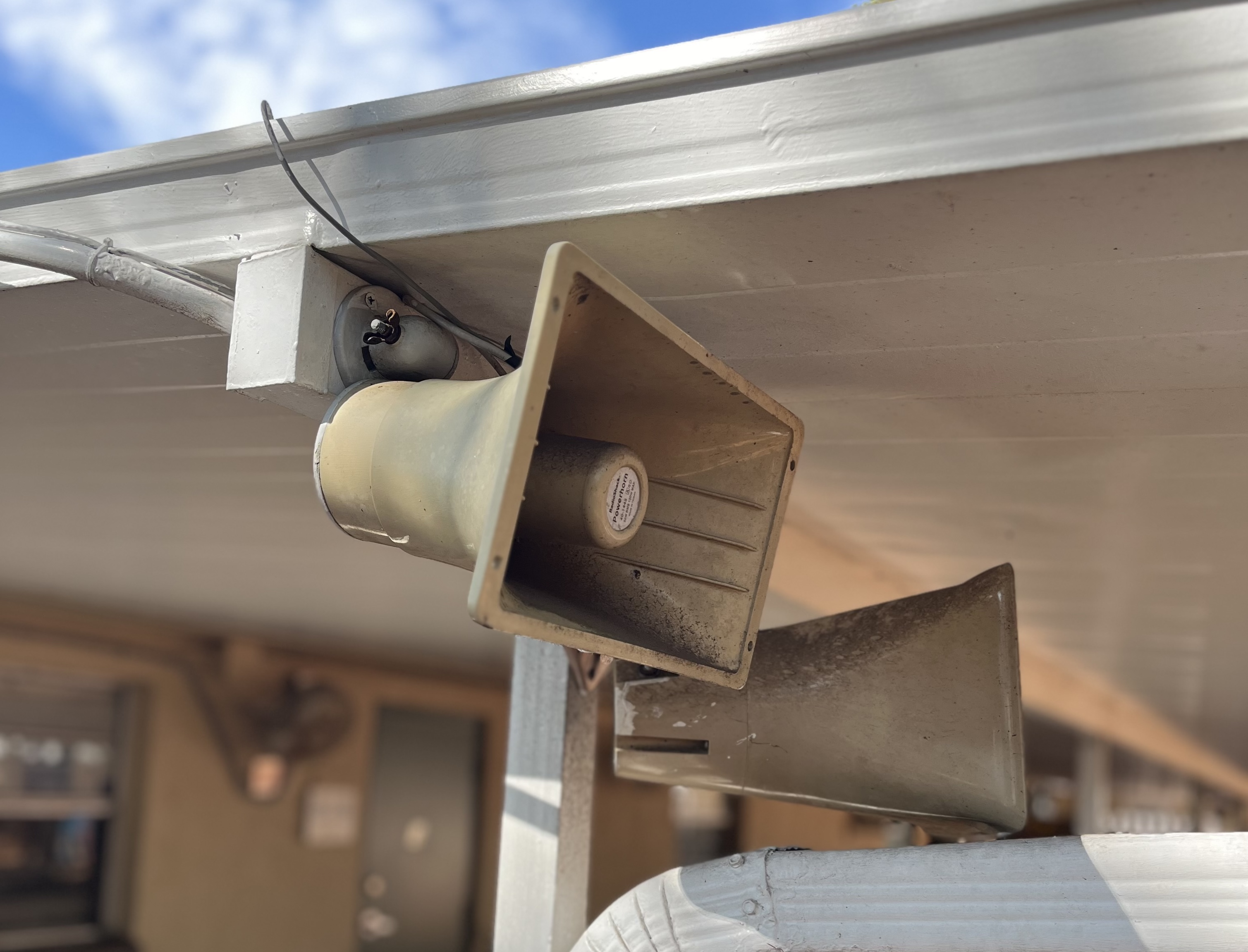 Two horn speakers mounted under the eave of a commercial building exterior.