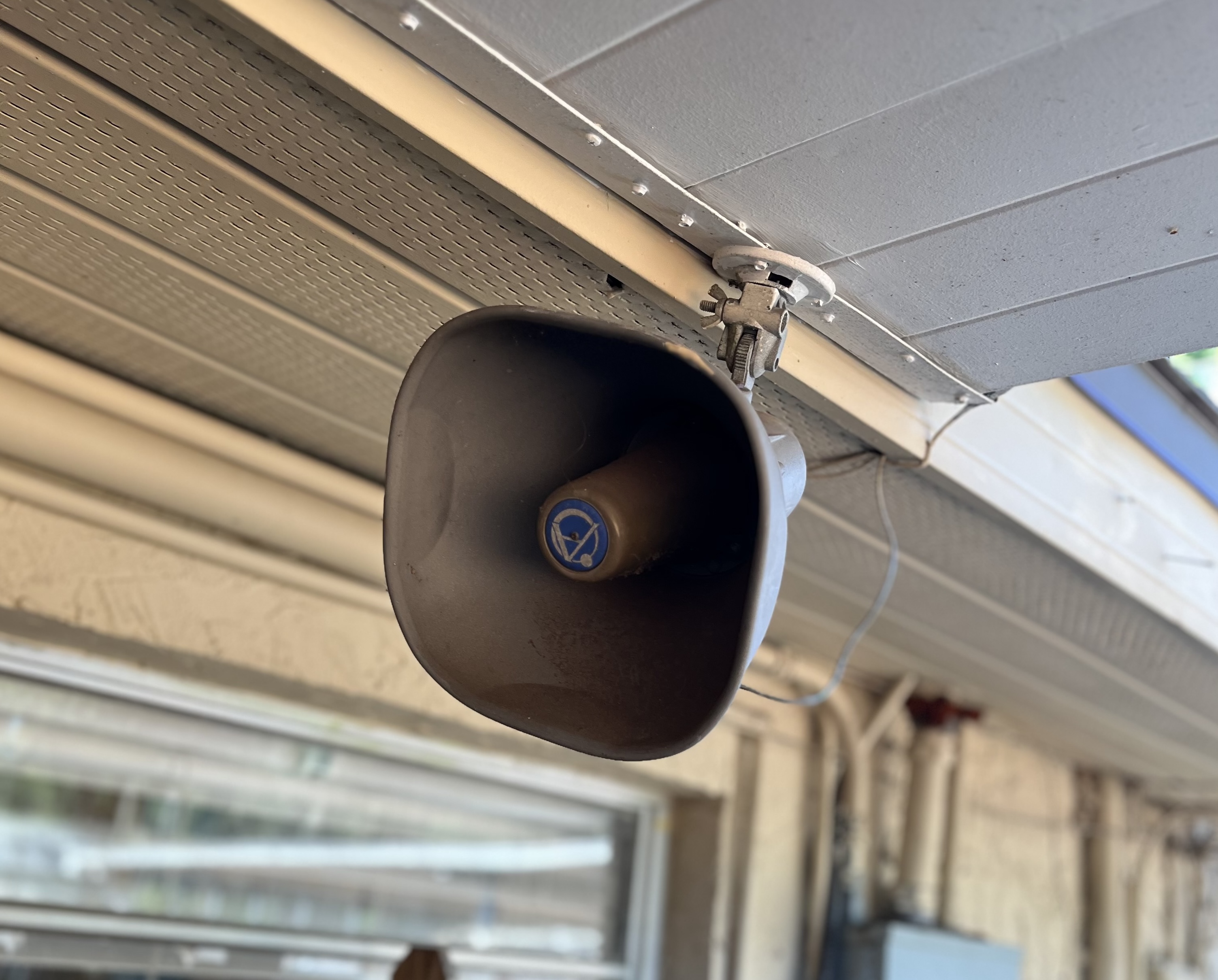 Horn speaker mounted to a soffit above a storefront walkway.