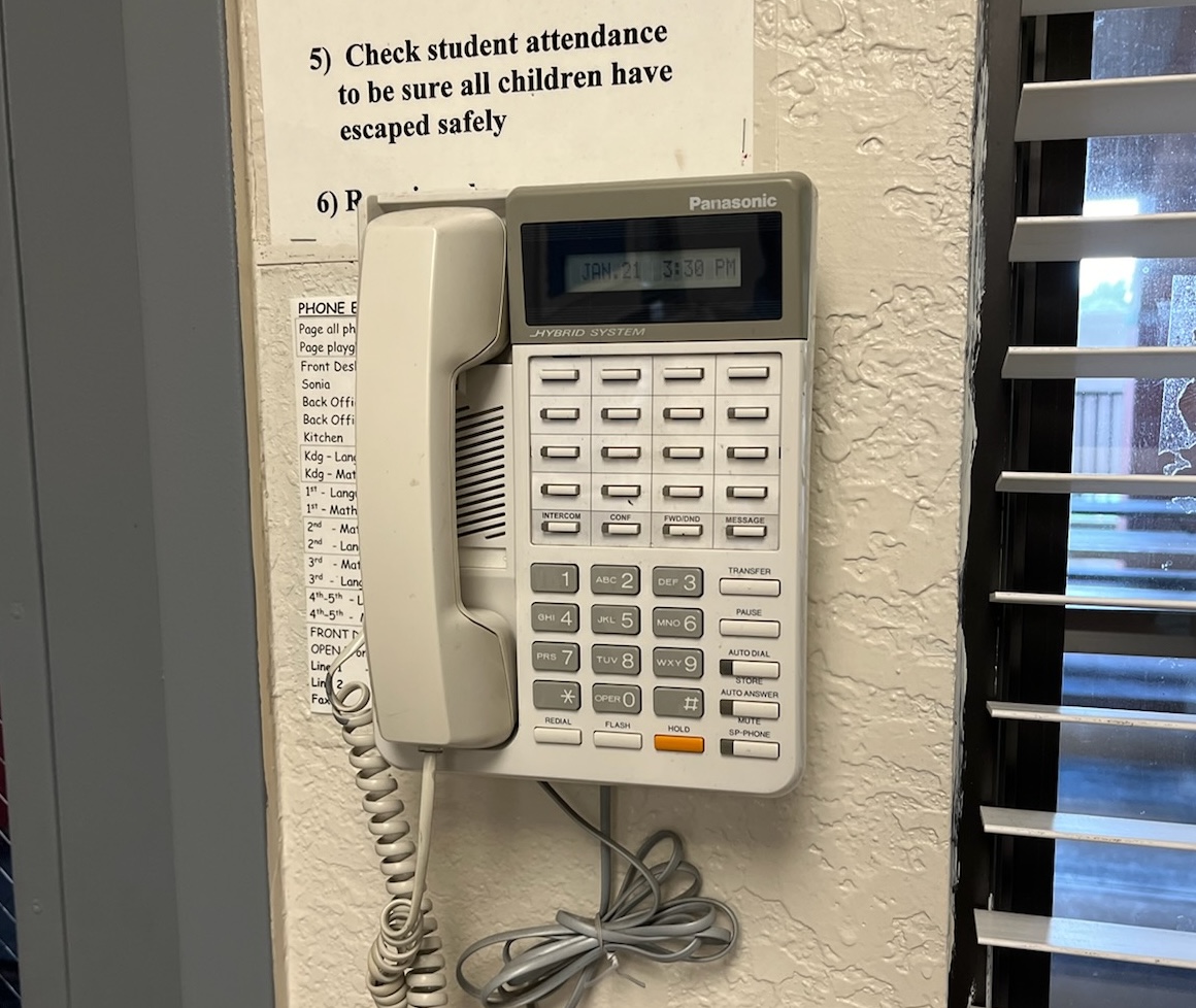 Wall-mounted Panasonic hybrid system phone beside a printed extension and paging directory.